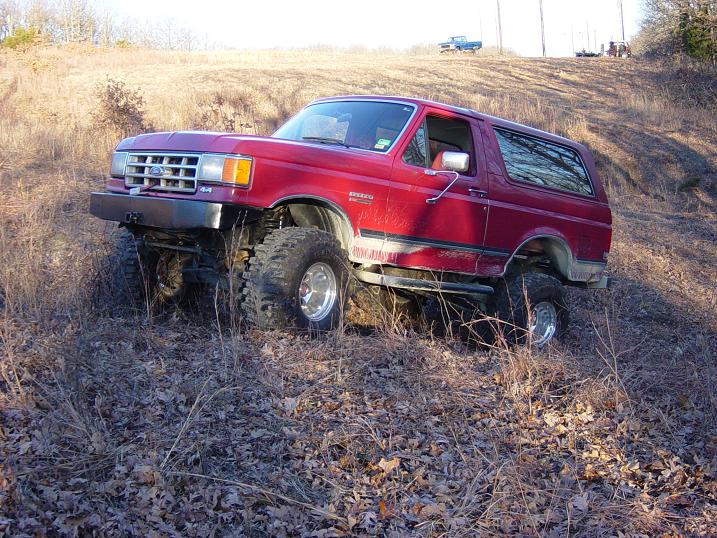 Red lifted Ford Bronco with big mud tires and chrome wheels parked on a brown grassy hillside
