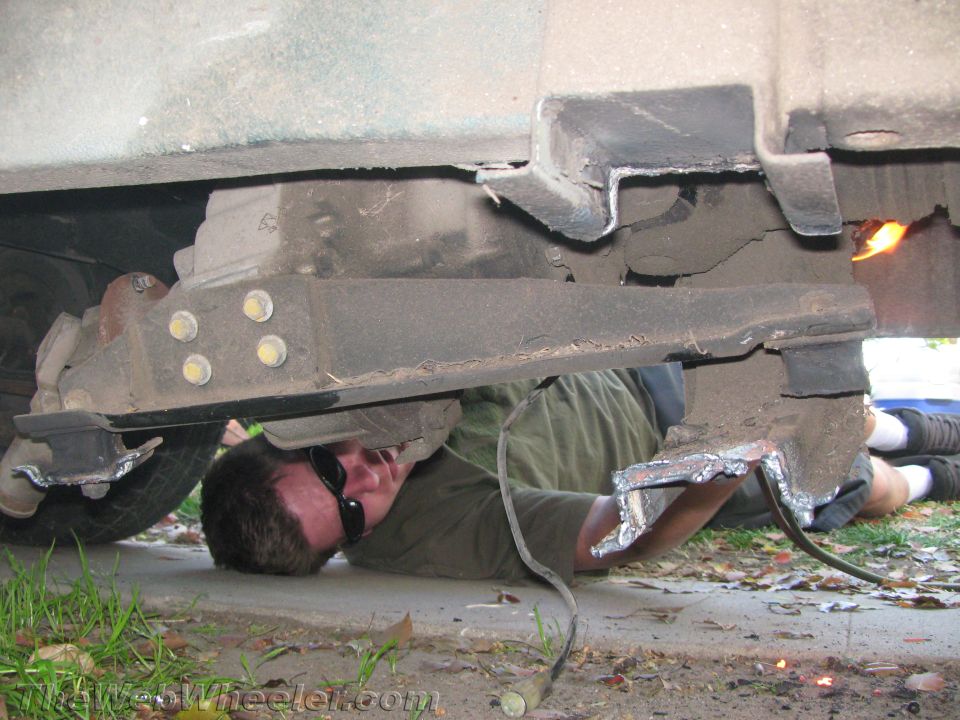 Guy welding on the frame of a vehicle while lying on the ground