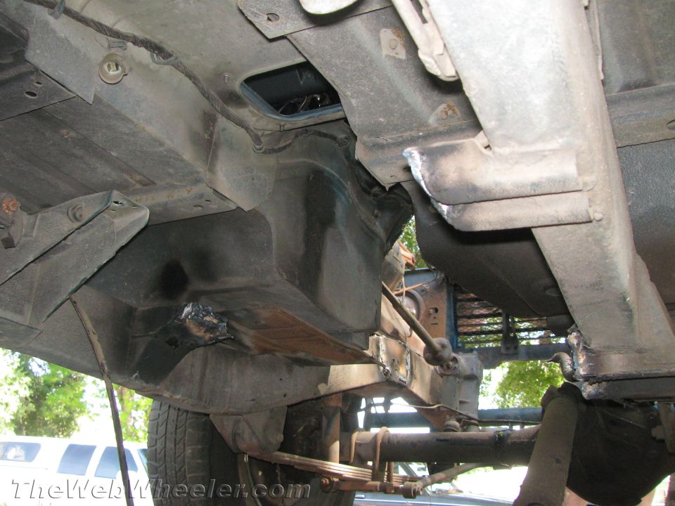 Underside of a vehicle showing frame, suspension, and leaf springs. Some welded repairs are visible