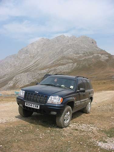 1991 Ford Crown Victoria - A dark blue Jeep Grand Cherokee is parked on a dirt road, with a large mountain range visible behind it.