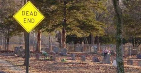 1991 Ford Crown Victoria - A dead end sign stands before a cemetery, with gravestones visible in the background.