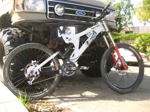 1989 Ford Bronco - A white downhill bicycle is parked in front of a tan Ford truck with oversized tires.