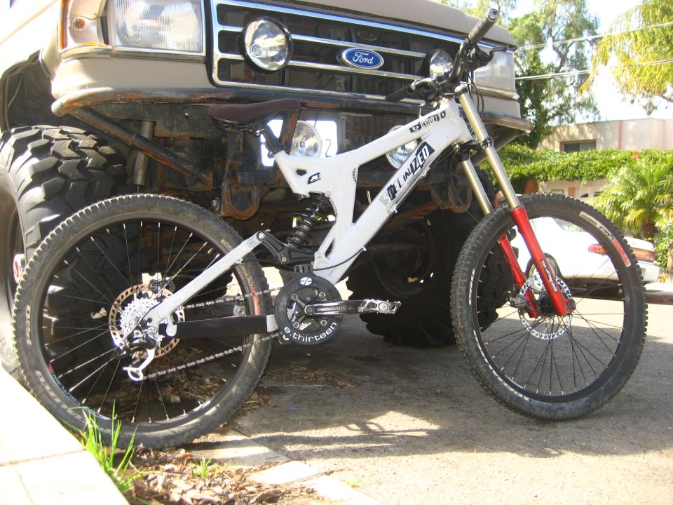 White downhill mountain bike leaning against the grille of a lifted tan Ford with big mud tires