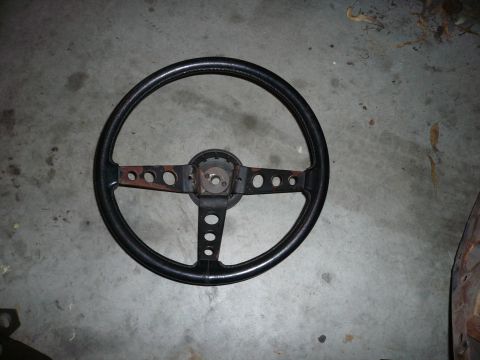 1975 Ford Ranchero - A black steering wheel with a three-spoke design, circular cutouts on the spokes, is shown against a concrete floor.