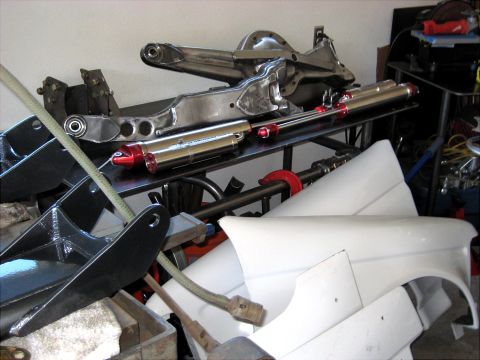 1996 Ford Bronco - Various automotive parts including a rear axle, shocks, and body panels are stored together.