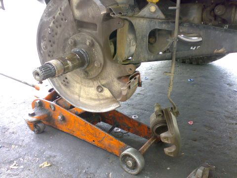 1995 Ford F-150 - Close-up of a vehicle's front wheel hub and brake system, supported by an orange hydraulic jack.