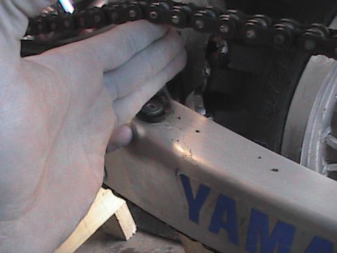 2007 Yamaha YZ450F - A hand adjusts the chain on a Yamaha motorcycle frame, with visible text and support blocks.