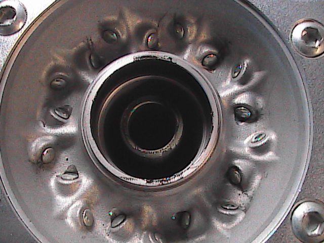 Close-up of a metal part with a central opening and a ring of bolts