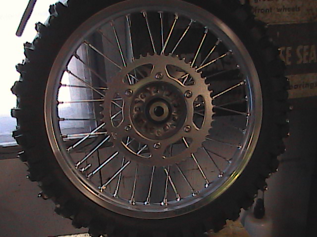 Motorcycle rear wheel with knobby tire and silver sprocket, close-up