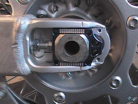 2007 Yamaha YZ450F - Close-up view of a motorcycle's rear wheel axle adjustment mechanism, showing the serrated adjuster and bolt.