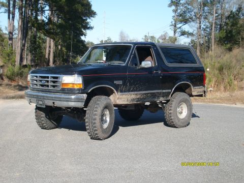 1992 Ford Bronco - This lifted black Ford Bronco is shown from a three-quarter front view on a paved road.