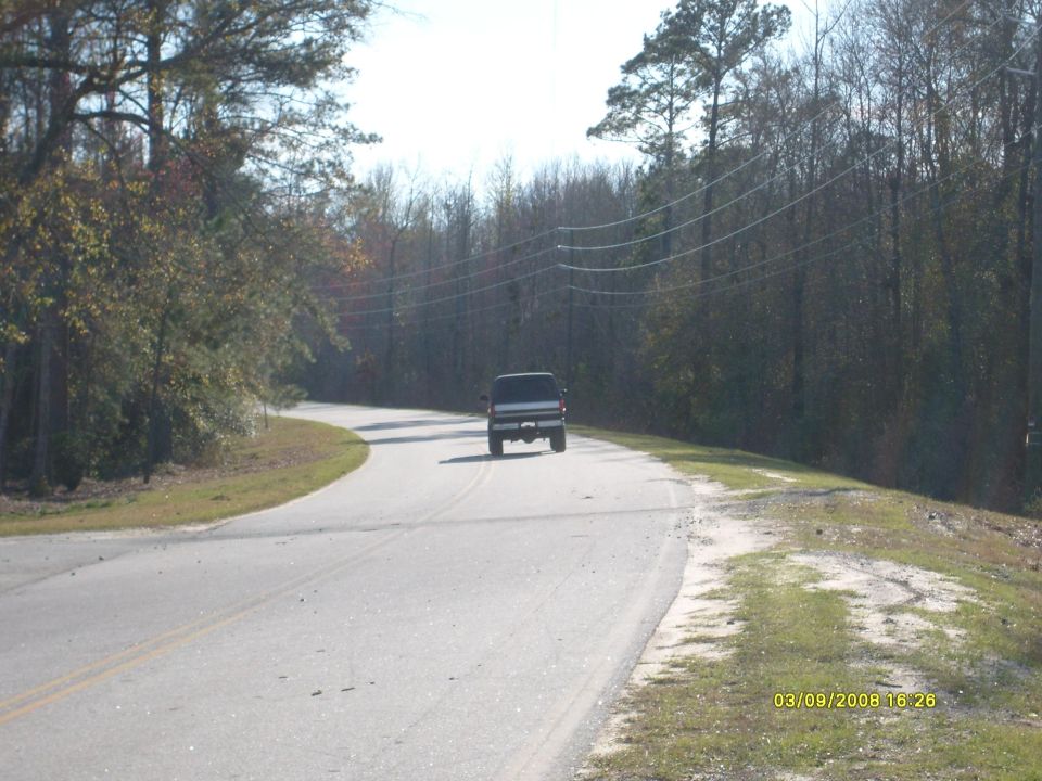 Dark pickup truck driving away on a rural two-lane road