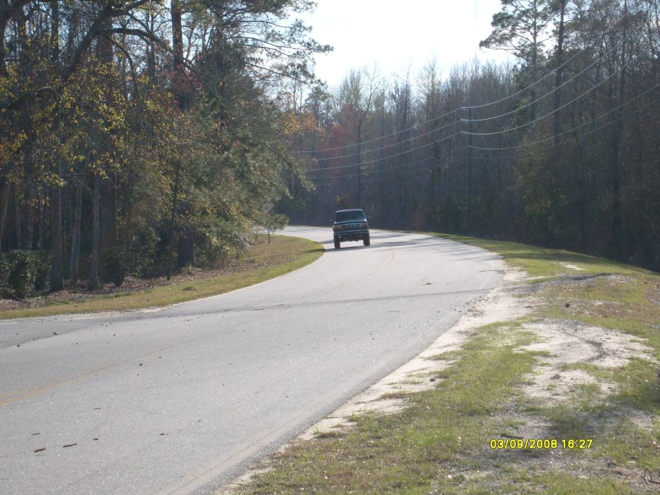 Dark SUV drives on a paved road through a wooded area