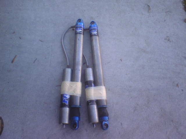 Two Fox shock absorbers with blue tops and silver bodies, taped with white tape