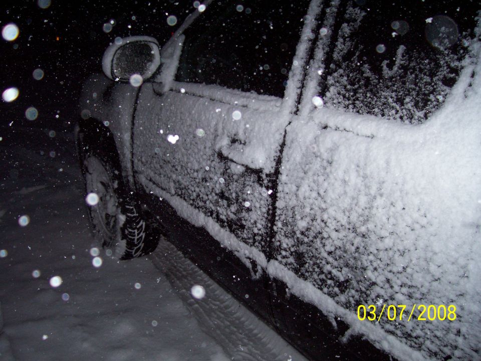 Side of a vehicle covered in snow at night. Date stamp shows 03/07/2008