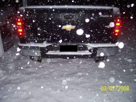 2008 Chevrolet Silverado 1500 - Rear view of a black Chevrolet Silverado pickup truck during a snowfall, showing its dual exhaust and gold bowtie emblem.