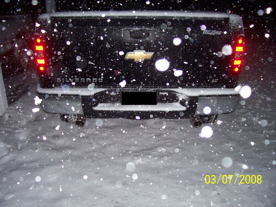 Black Chevrolet Silverado pickup truck rear in snow, dual exhaust pipes, gold bowtie emblem