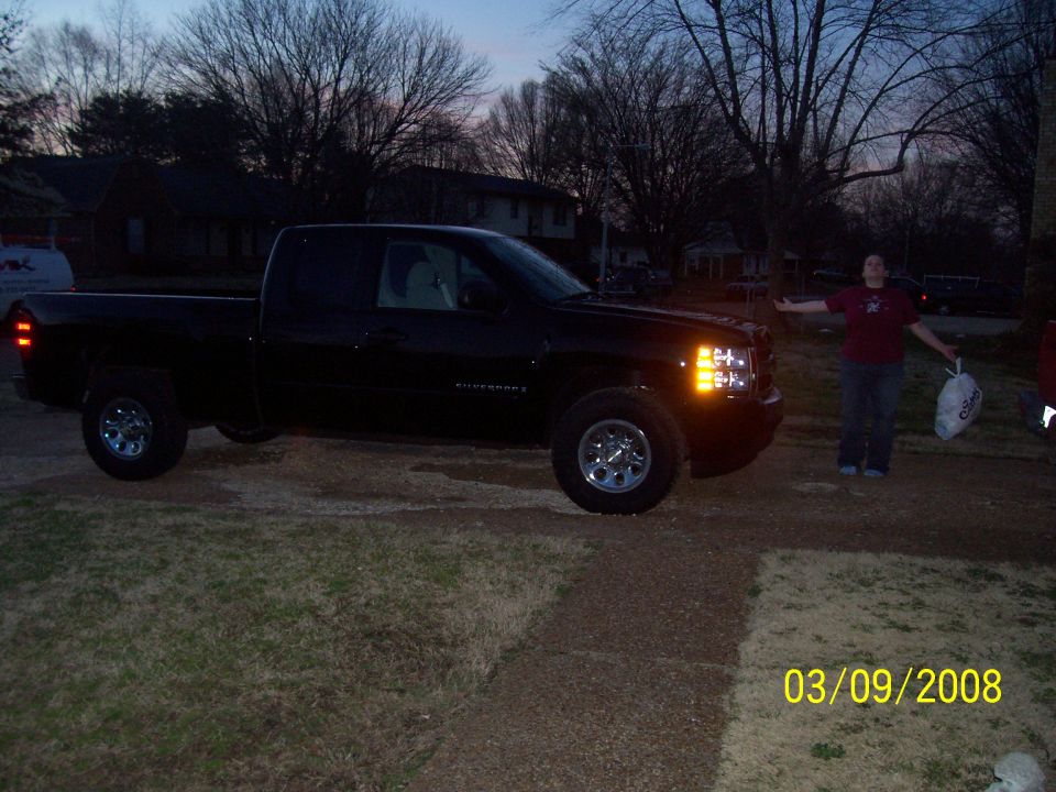 Black pickup truck parked outside at dusk. A person stands to the right of the truck with arms outstretched