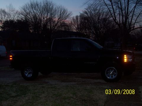 2008 Chevrolet Silverado 1500 - A black 2008 Chevrolet Silverado 1500 is parked in a grassy area at dusk, with trees and houses in the background.