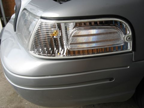 2004 Ford Crown Victoria - Close-up of a silver car's front corner, highlighting the clear turn signal and ribbed headlight assembly.