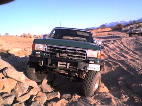 1991 Ford Bronco - Green 1991 Ford Bronco tackling a challenging off-road trail with mountains in the distance.