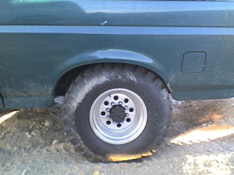 1991 Ford Bronco - The rear side of a green Ford Bronco shows a flat tire and a fuel door.