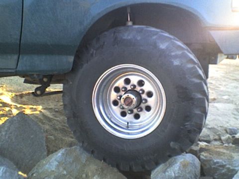 1991 Ford Bronco - The side profile of a dark blue 1991 Ford Bronco is visible, a large tire and wheel assembly.
