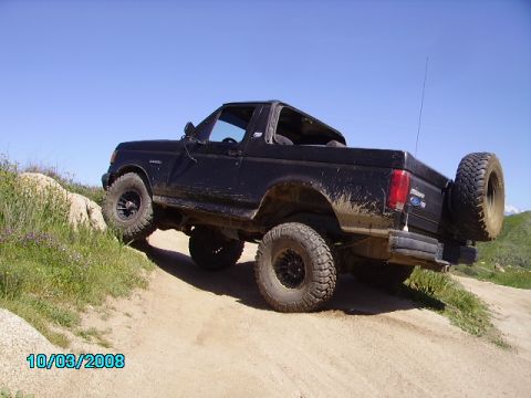 1990 Ford Bronco - This SUV is navigating a dirt trail with a rocky incline under a clear blue sky.