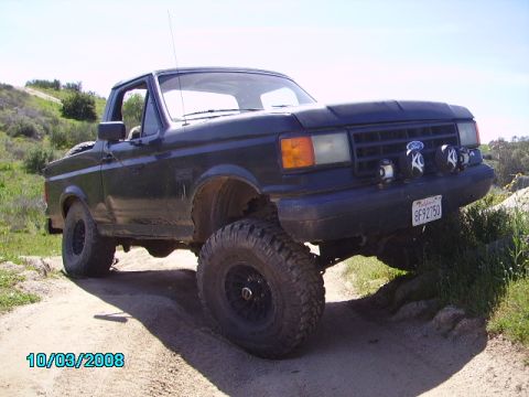 1990 Ford Bronco - A modified 1990 Ford Bronco navigates a rocky, off-road path with its front wheels elevated.
