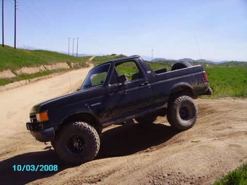 1990 Ford Bronco - This black 1990 Ford Bronco is captured in a 3/4 front view on a dusty, off-road trail.