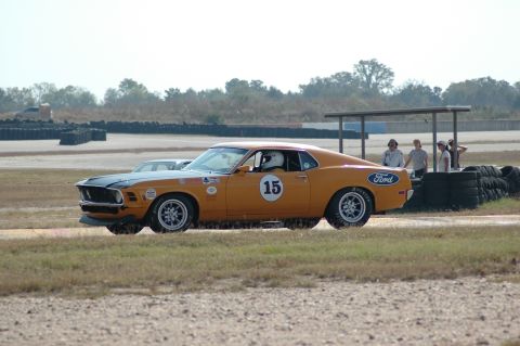 1970 Ford Mustang - This orange 1970 Ford Mustang race car, identified by its body style and number 15 on the door, is captured in a side view on a track.