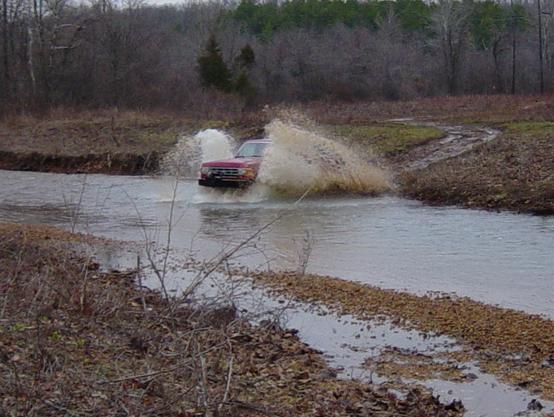 Pickup truck blasting through a creek crossing throwing a large wall of water spray