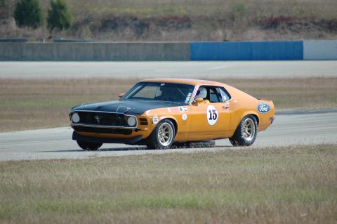 1970 Ford Mustang - A 1970 Ford Mustang race car with a black hood and orange body is captured on the track.