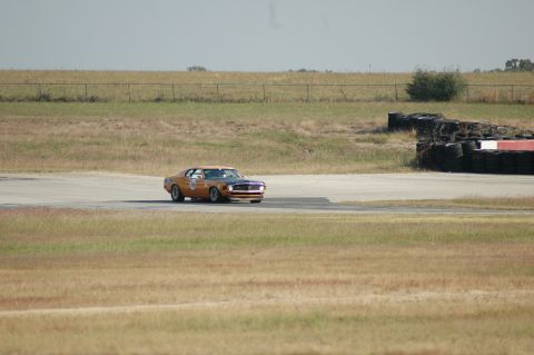 1970 Ford Mustang - A 1970 Ford Mustang, identified by its body style and racing number 25, navigates a turn on a sunny day at the racetrack.
