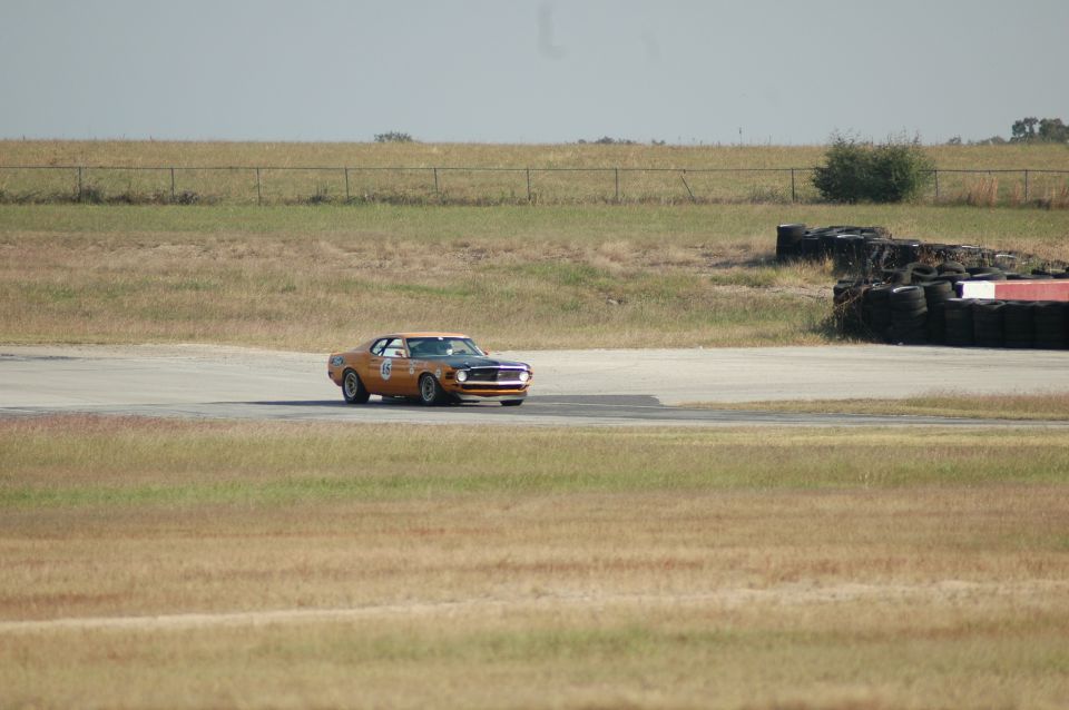 Distant orange No. 15 Mustang race car rounding a corner past a tire barrier