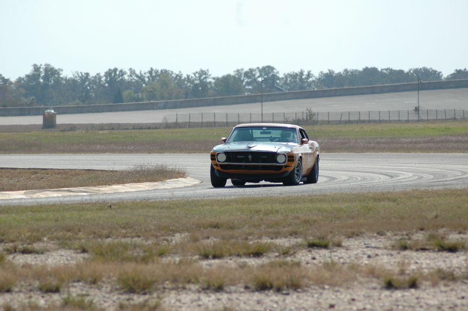 Orange Mustang race car head-on down a straight, twin headlights and pony grille