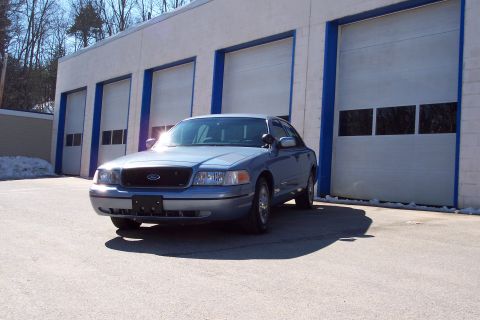 2001 Ford Crown Victoria - A blue 2001 Ford Crown Victoria is parked outside a building with multiple garage bays.