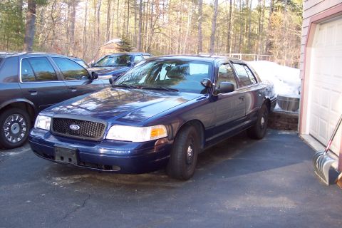 2001 Ford Crown Victoria - Two Ford Crown Victoria police cars are parked in a driveway next to a garage with snow in the background.