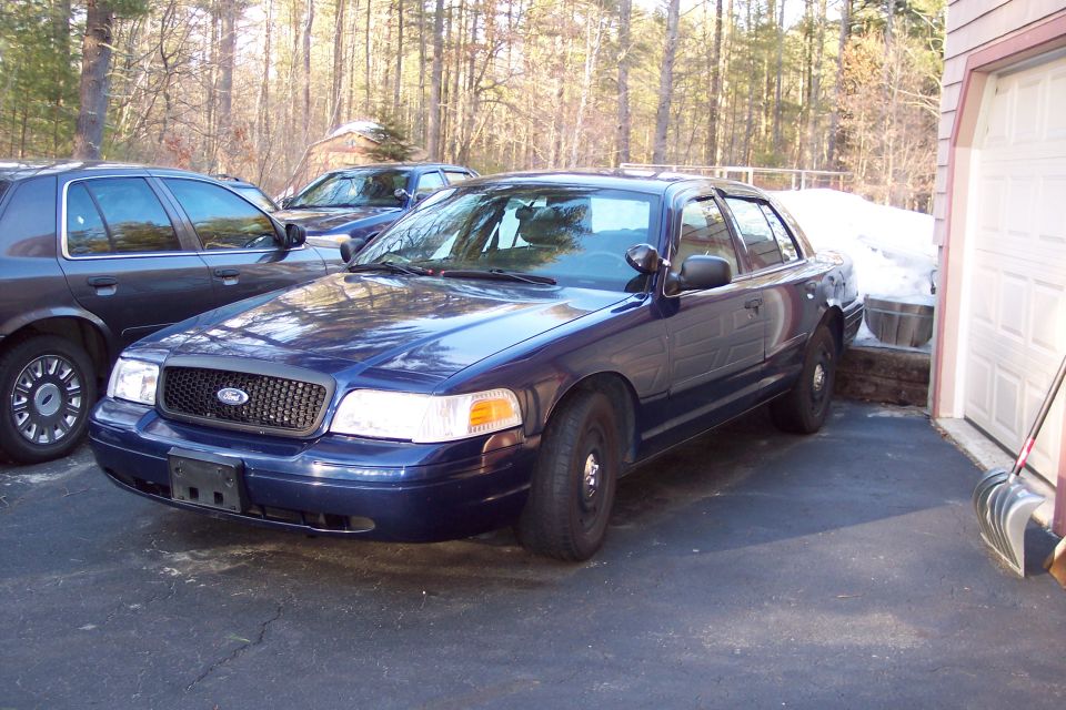 Dark blue 2001 Ford Crown Victoria police car parked next to a garage, another similar car behind it