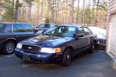2001 Ford Crown Victoria - Two dark blue Ford Crown Victorias are parked in a driveway with snow visible near a garage.