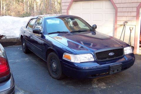 2001 Ford Crown Victoria - A blue 2001 Ford Crown Victoria is parked in front of a garage door.