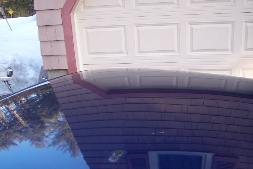 Reflection of trees and sky on a dark car roof in front of a white garage door