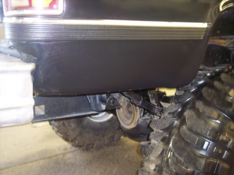 1984 GMC Sierra 3500 - Close-up of a black pickup truck's rear fender and massive tire, revealing suspension components and a portion of the taillight assembly.