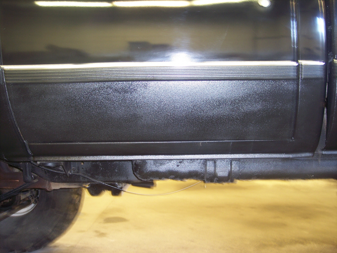 Black textured coating on the lower door and rocker panel of a black pickup in a shop