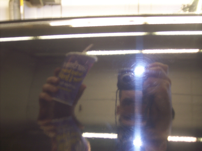 Reflection of a person holding a cup and a camera in a dark, reflective surface