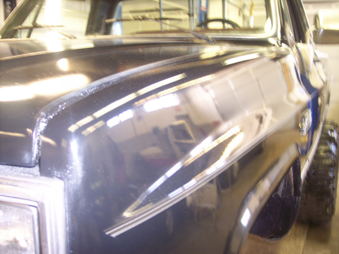 Glossy dark blue fender and hood of a square-body pickup in a shop