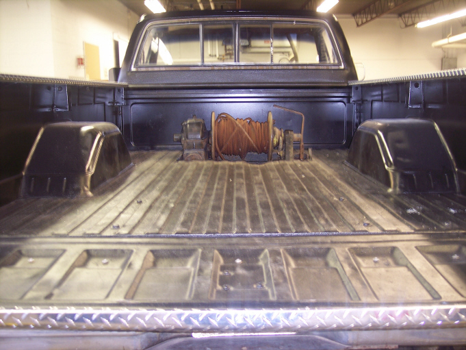 Empty black pickup bed with a rusty cable winch at the headboard, viewed over the tailgate