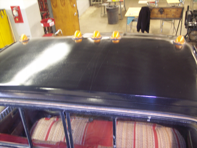 Glossy black truck cab roof with five amber marker lights, red striped bench seat below