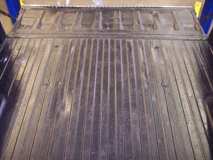 Empty ribbed truck bed with tailgate down on a vehicle lift