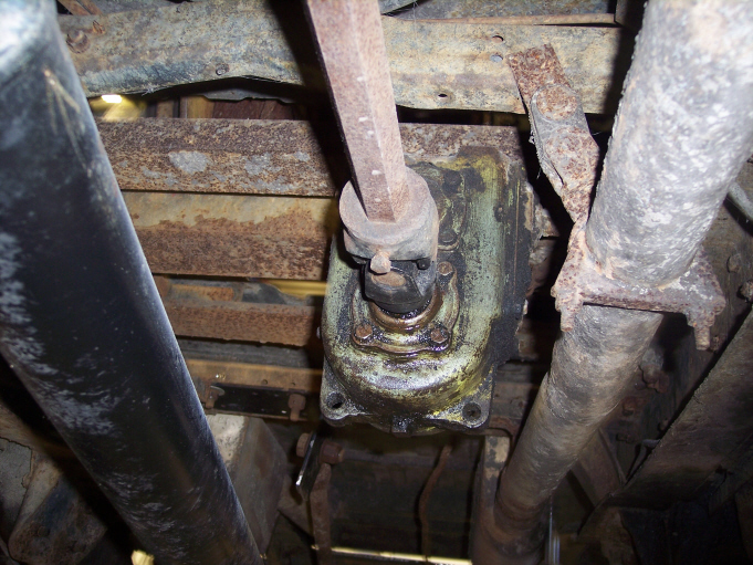 Greasy steering gearbox bolted to a truck frame rail seen from underneath